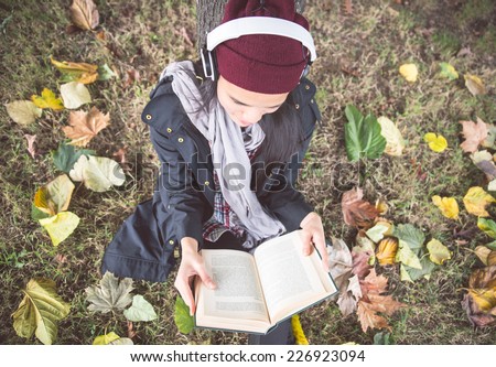 woman reading book in the nature listening to music with headset. autumn concept