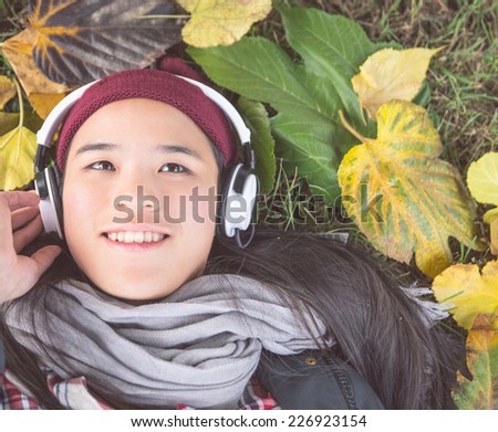 woman listening to music in a garden with autumn leafs on the ground. seasonal concept about autumn