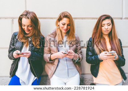 Girls typing on mobile phones - Three friends holding mobile phones and chatting - Youth,technology and communication concepts