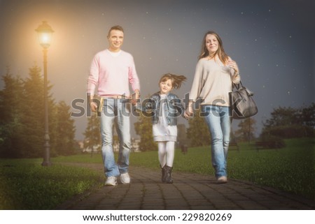 Happy beautiful family walking in a park - Mom and dad taking pretty daughter by hand