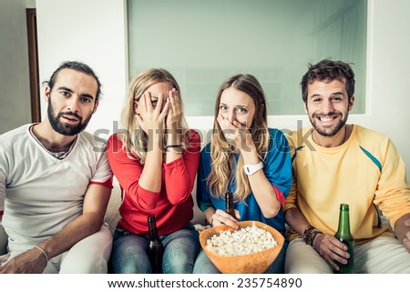 friends watching horror movie at television. different reaction on their faces