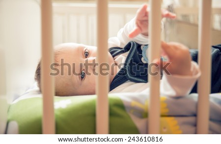 Portrait of playful baby with blue eyes in his bed - Candid image of young boy playing at home
