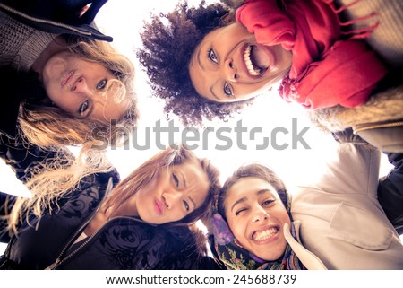 Group of attractive young women of different ethnics hugging in a circle - Four students smiling at camera - Best friends spending time together