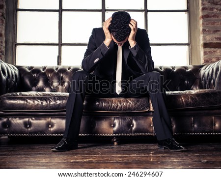 Depressed business man sitting on sofa - Negative image of young sad person