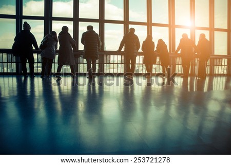 Silhouette of the tourists at transparent viewing observatory - People watching at window at sunset - Travelers waiting flight at airport