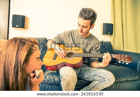 Young man playing guitar for his girlfriend at home - family,recreation,leisure,togetherness concept