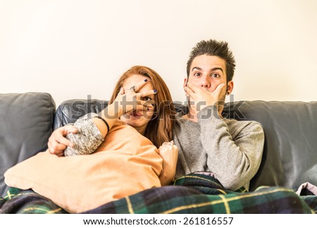 Couple watching horror movie on television on the couch - Young  man and woman sitting on the couch and looking at tv in shock- family,recreation,leisure,togetherness concept