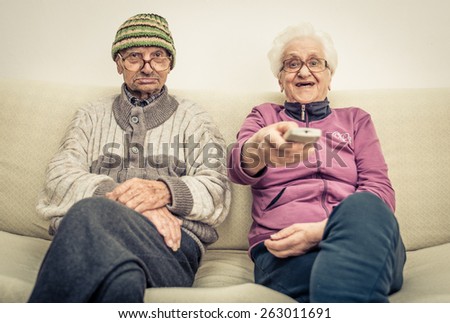 old couple watching television on the couch in the living room. concept about aging, old people, entertainment, humor and people