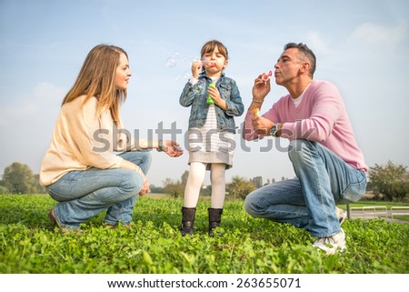Portrait of happy family - Pretty young girl playing with soap bubbles in a park with her parents