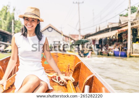 Beautiful asian woman visiting the Floating Market in Bangkok on a boat tour - Asian tourist smiling and looking at camera on a typical thai boat