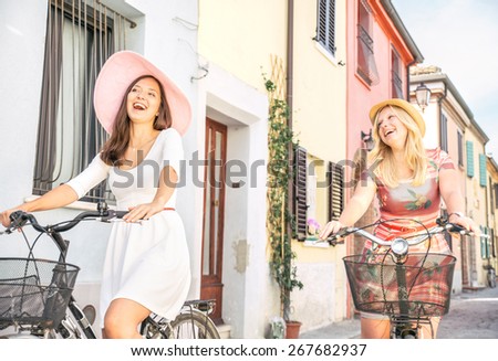 Happy couple riding bikes in the city - Two girlfriends on bikes talking and laughing - Best friends spending time together on vacation