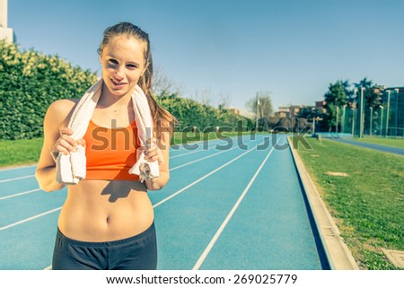 Young female athlete on a running track with a towel after hard training - Beautiful caucasian woman relaxing after running in a sport centre - Concepts about sport,wellness and recreation