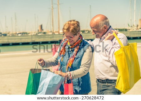 Senior couple shopping - Two mature persons with colored shopping bags walking on the streets at a sale event - Wife showing presents for family at her husband