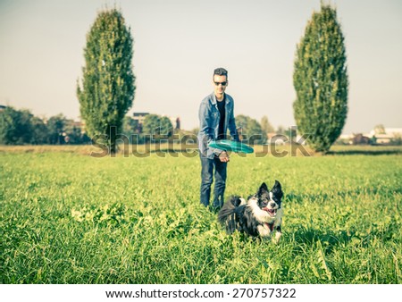 Cool dog and young man having fun with frisbee in a park - Australian shepherd dog running  and trying to catch a frisbee - Concepts of friendship,pets,togetherness.Focus on frisbee