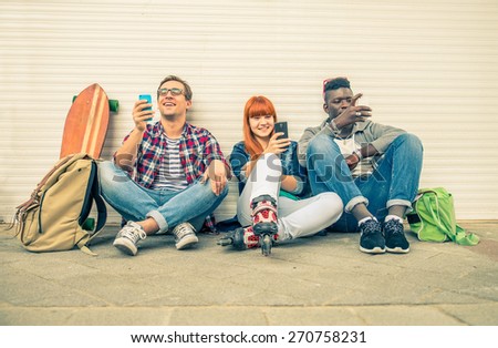 Group of friends of different ethnics sitting on the street and looking at phone - Young hipster people having fun with new technologies - Multiracial group representing the addiction to technology