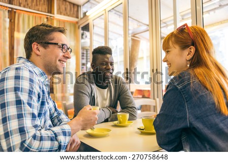 Friends talking and smiling in a coffee house - Group of young multiracial students meeting in a bar and drinking coffee - Happy cheerful persons in a restaurant