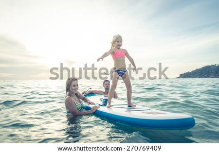 happy family teaching the daughter to stand on the surf in the ocean. concept about family, sport, active people
