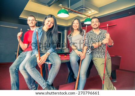 Two couples having fun at billiard - Group of multiracial young people standing next to pool table and holding cue - Students spending an evening at pub