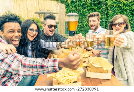 Group of mult-ethnic friends toasting beer glasses - Happy people partying and eating in home garden - Young active adults in a picnic area with burgers and drinks