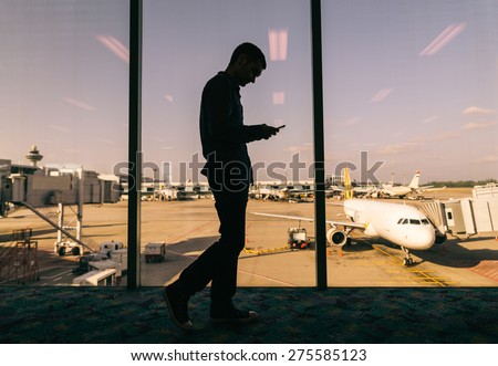 Young man checking his phone while waiting his flight in the airport - Business man at airport and airplane and airport in the background