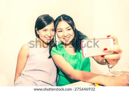 Two girlfriends taking a selfie with smart phone - Happy women having fun at party - Young multiracial couple of girls sending their photo to friends with wireless internet