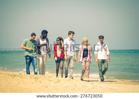 Multi-ethnic group of friends walking on the beach and talking - Group of young adults silhouettes outdoors at sunset