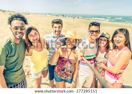 Multiethnic group of friends enjoying vacation  and taking a picture with selfie stick - Mixed group of several people having fun on the beach