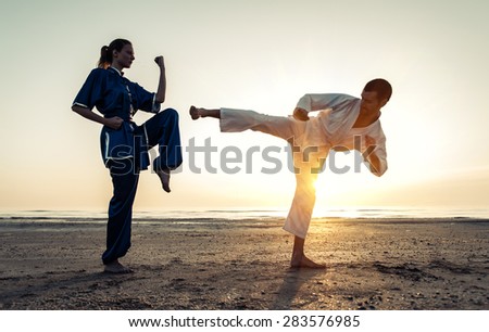 couple training in martial arts on the beach at sunrise. karate kick versus wu shu parry. concept about martial arts