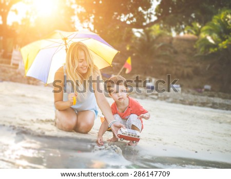 mom and kid playing on the beach. mom playing with toys car with her little son
