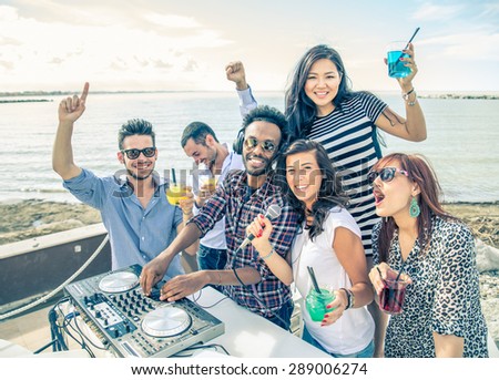 Dj playing trendy music in a open air club - People dancing and partying while the disc jockey mixes two song tracks at at summer concert