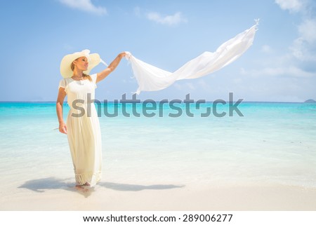 Beautiful woman with long white dress and hat walking on a tropical beach with crystalline water - Fashion model in a idyllic vacation resort