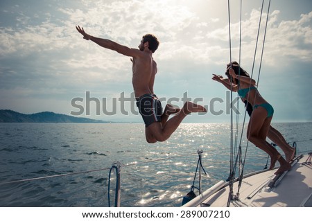 Silhouettes of happy people jumping into water from a boat - Friends diving and having fun on a summer vacation