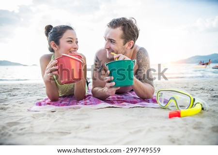 Couple of lovers on vacation drinking cocktails in party bucket and having fun - Two friends tanning on the beach while talking and laughing