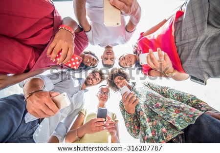 Group of multiethnic people in circle looking down at smartphones - Young people of diverse ethnics playing with new technologies