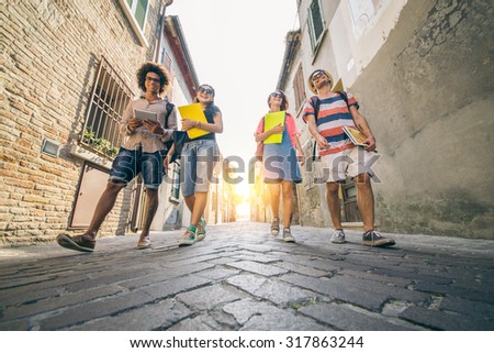 Group of multi-ethnic students talking and laughing while going to university - Four happy friends walking outdoors