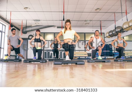 Group of sportive people training with step in fitness club - Aerobics class in a gym, coach showing legs exercise