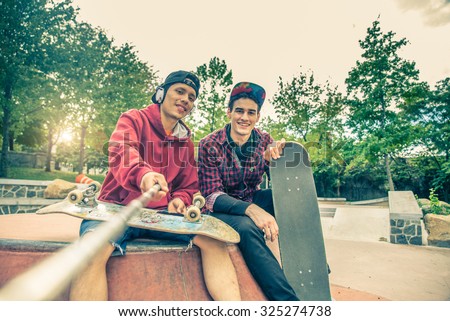 Two young men in a skate park holding a selfie stick and photographing themselves - Two skaters having fun on a skate competition