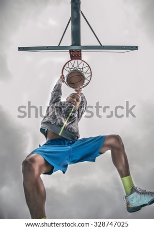 Sportive man hanging from the basket and looking down triumphant at camera after a slam dunk - Basketball player scoring for his team