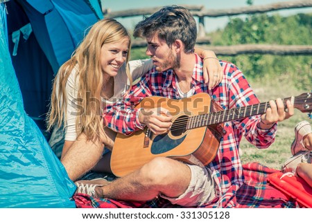 Couple in a camping site playing guitar and singing - Lovers on a week end vacation in the nature