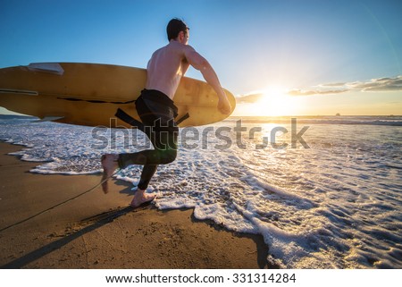 Surfer with board running into the the ocean at sunset - Sportive man going to surf on a tropical beach