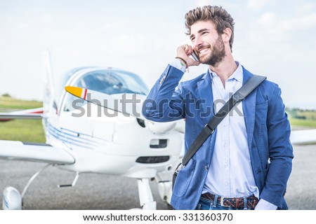 Business man with his airplanes. He is walking in the airport with the smart phone and making a call.