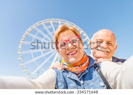 Senior couple taking a selfie at amusement park - Two persons in the 60\'s having fun with new technologies outdoor
