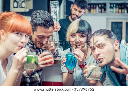 Friends having cocktails in a bar. Barman preparing drinks in the background. Fun, job and people concept