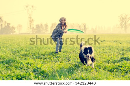 Young beautiful girl throwing frisbee to her dog in a park at sunset - Asian woman playing with her dog