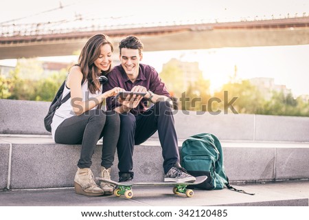 Beautiful couple sitting on a bench outdoors and looking at tablet - Lovers having fun with new technology and shopping online