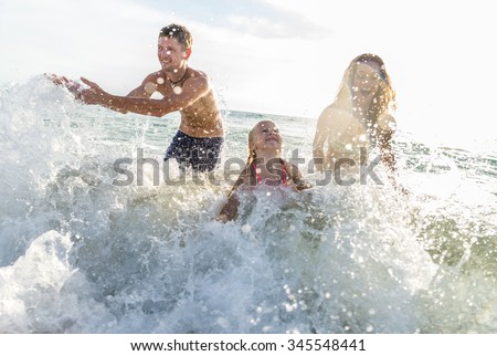 Happy family playing in the ocean and splashing water - Tourists on vacation on a tropical island