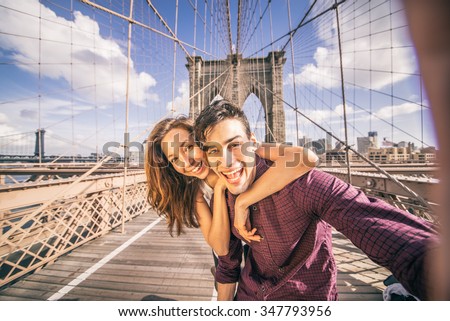 Beautiful couple taking selfie on Brooklyn Bridge, New York - Tourists having fun and photographing NY landmarks