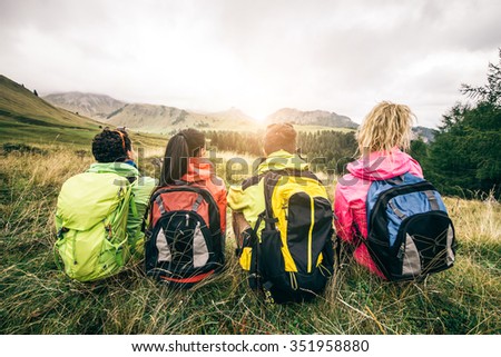 Four backpackers looking at sunset over the mountains - Hikers talking and relaxing after an excursion in the nature - Friends enjoying winter holiday