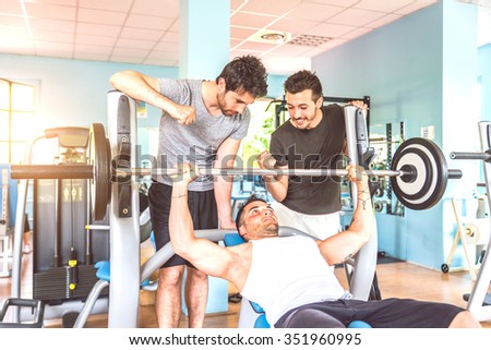 Sportive man lifting weight in a gym - Coach inciting a body builder to finish his work out - Three friends working out in a weights room