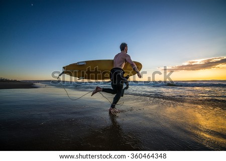 Surfer running into water with surf board at sunset